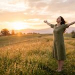 Versículo sobre descanso em Deus — Mulher de braços abertos ao pôr do sol representando paz e descanso em Jesus — Mateus 11:28-30